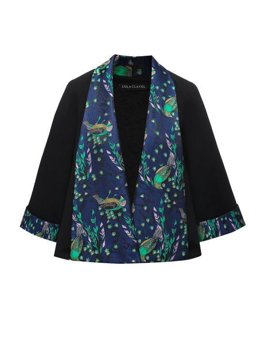 Front view of a reversible black brocade kimono-style jacket with wide sleeves and a rich blue jacquard lining featuring birds and foliage in green and violet tones, designed by Lola Clave